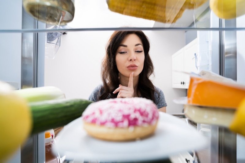 Confused Woman Thinking Looking At Sweets In Fridge